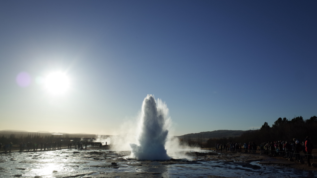 Geysir erupting in Iceland surrounded by crowds.