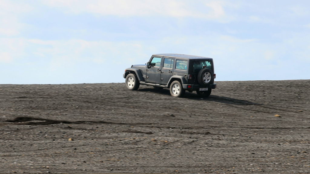 Jeep driving on black sand beach in Iceland.