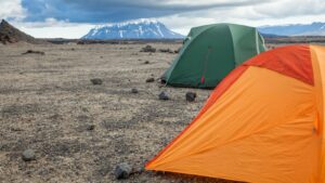 Orange and green camping tents on rocky ground in Iceland with Herðubreið volcano in the distance.